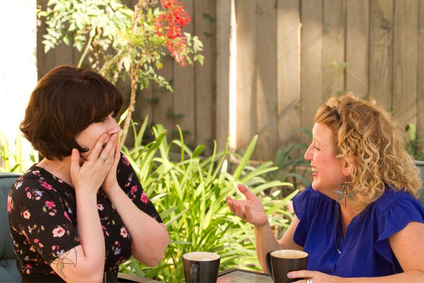 Spreche mit Menschen, die dich inspirieren und motivieren, anstatt dich in negativen Gesprächen über Geldsorgen zu verlieren. Zwei Frauen, die sich bei einer Tasse Kaffee unterhalten.