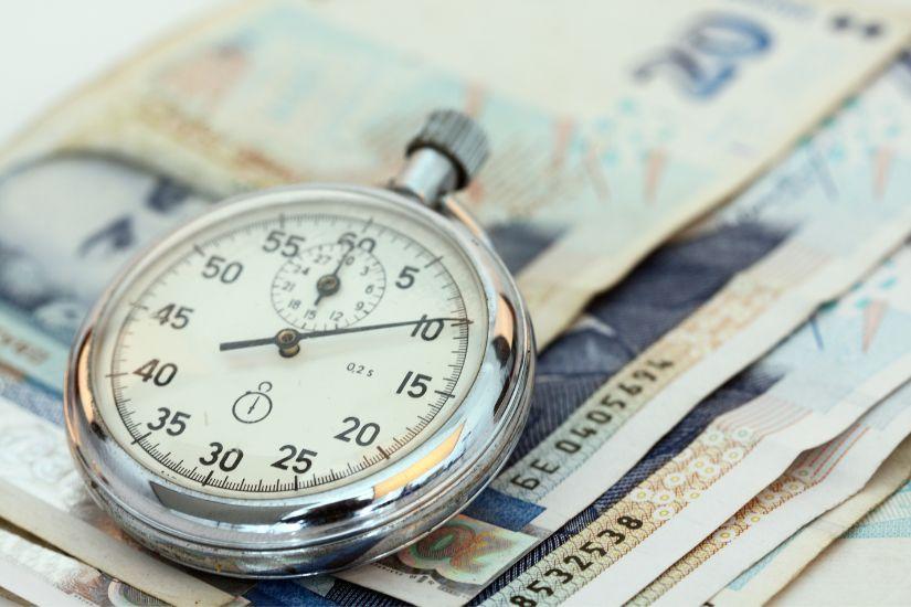 Deshalb sind pünktliche Zahlungen der wichtigste Faktor für eine gute Bonität. Stelle also sicher, dass du alle Rechnungen rechtzeitig begleichen kannst, um Zahlungsausfälle zu vermeiden. Eine Uhr mit Geldscheinen.