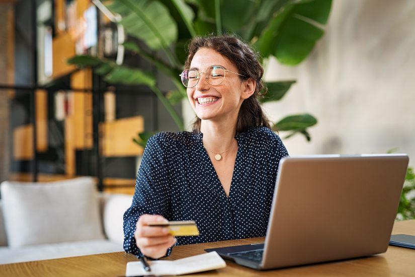 Daher solltest du wie beim Girokonto regelmäßig prüfen, wie viele Kreditkarten du tatsächlich benötigst. In der Regel haben ein bis zwei Kreditkarten einen positiven Einfluss auf deine Bonität, mehr eher nicht. Eine lächelnde Frau am Computer, die nur eine Kreditkarte besitzt.